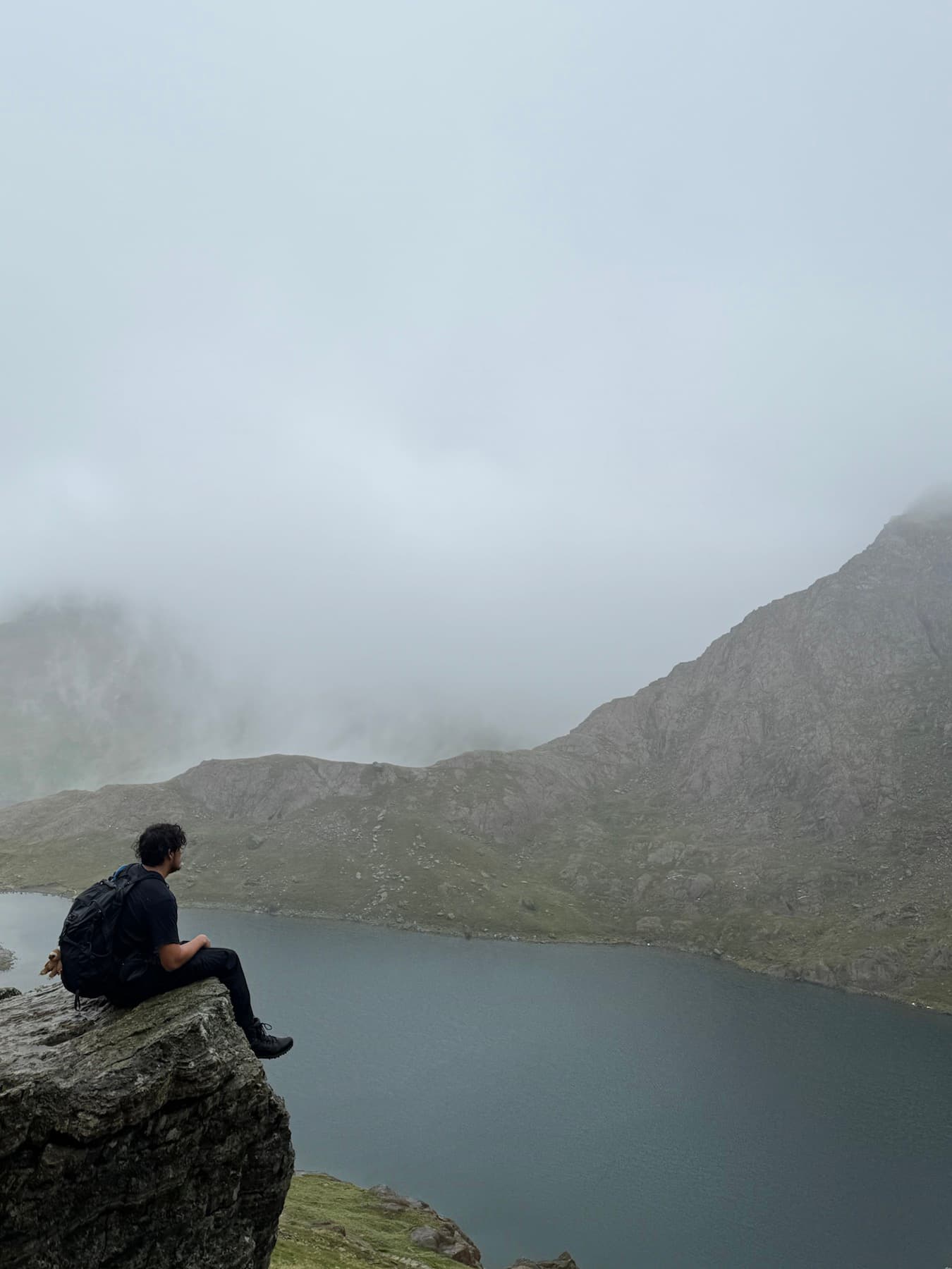 Brian sitting on a cliff above a misty mountain lake